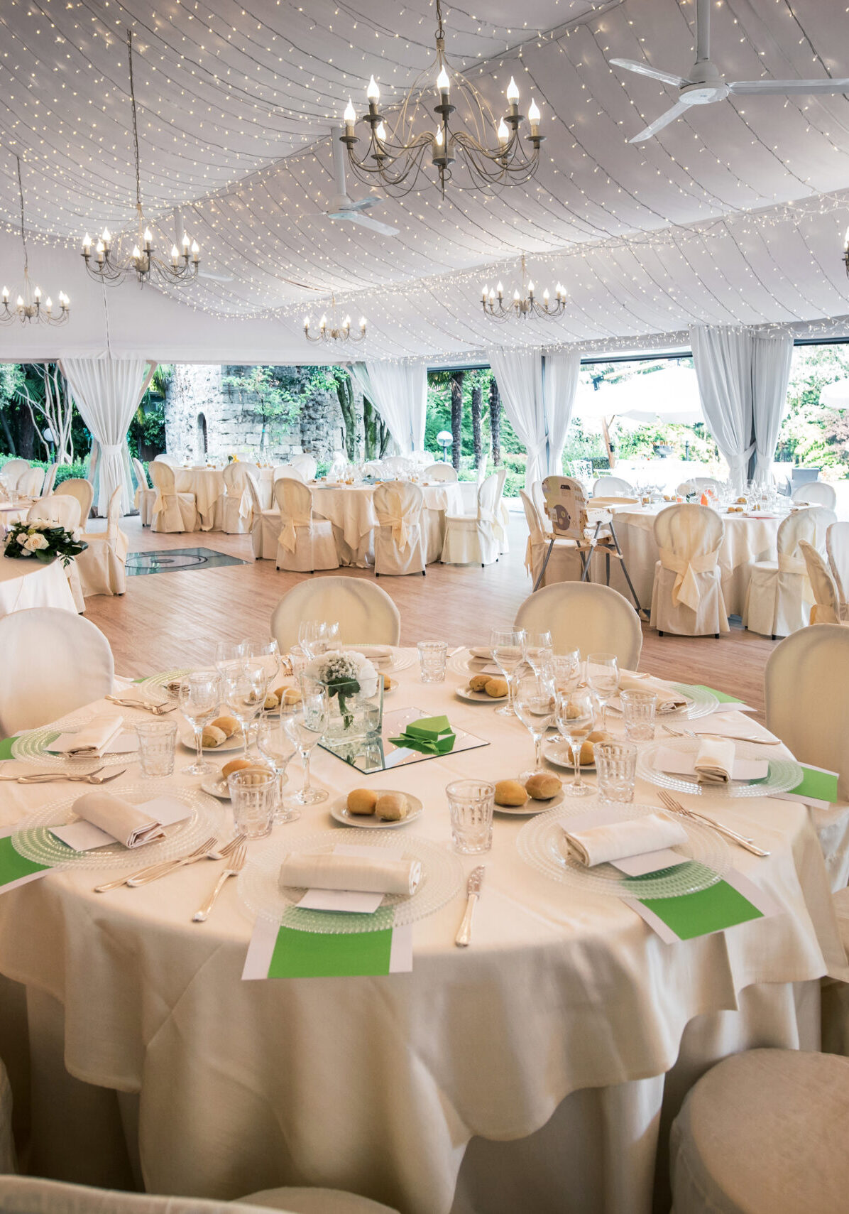Wedding reception venue in a large marquis with elegant formal white table settings and a view of a garden