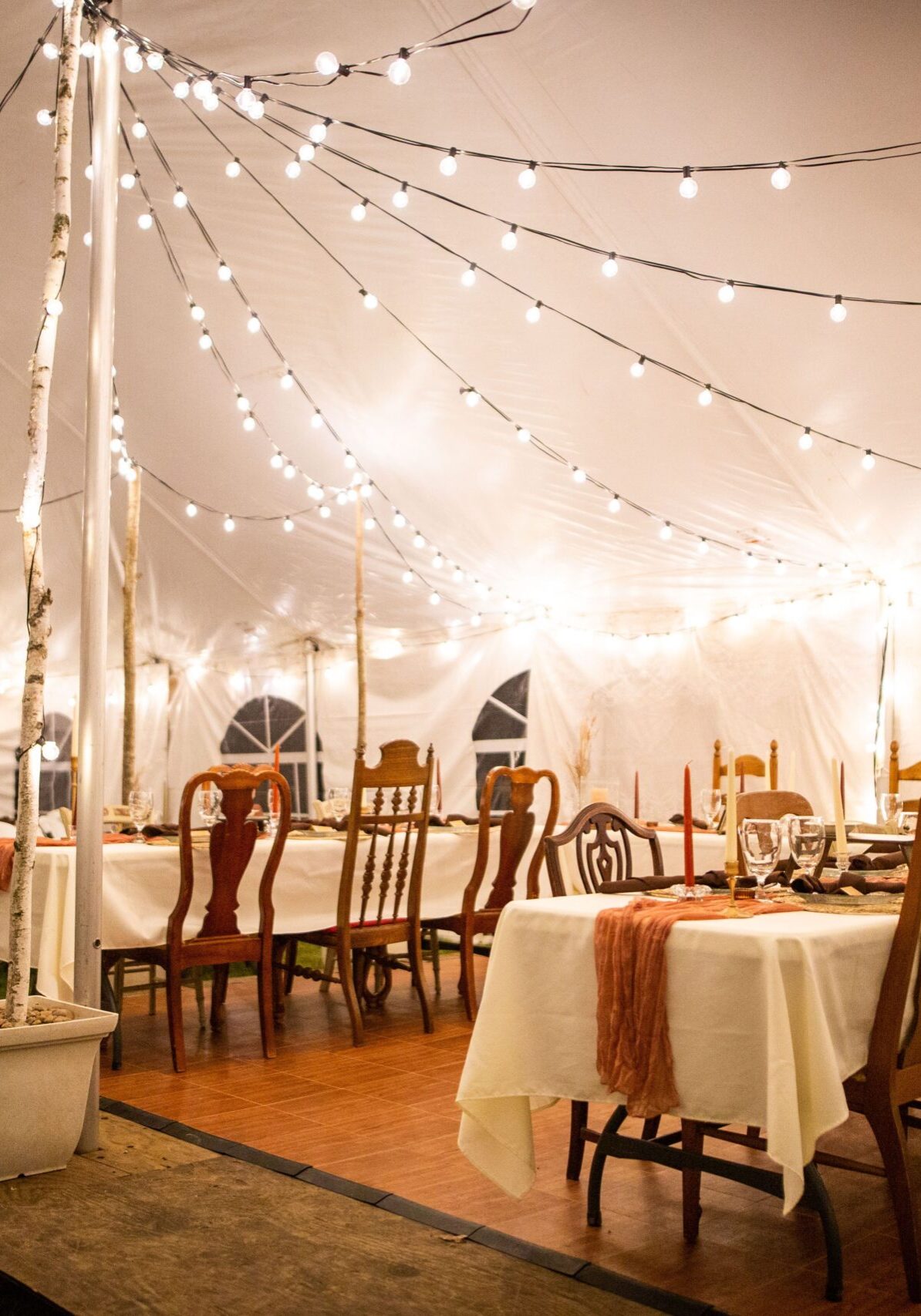 A wedding venue tent with dinner equipment on tables and string lights